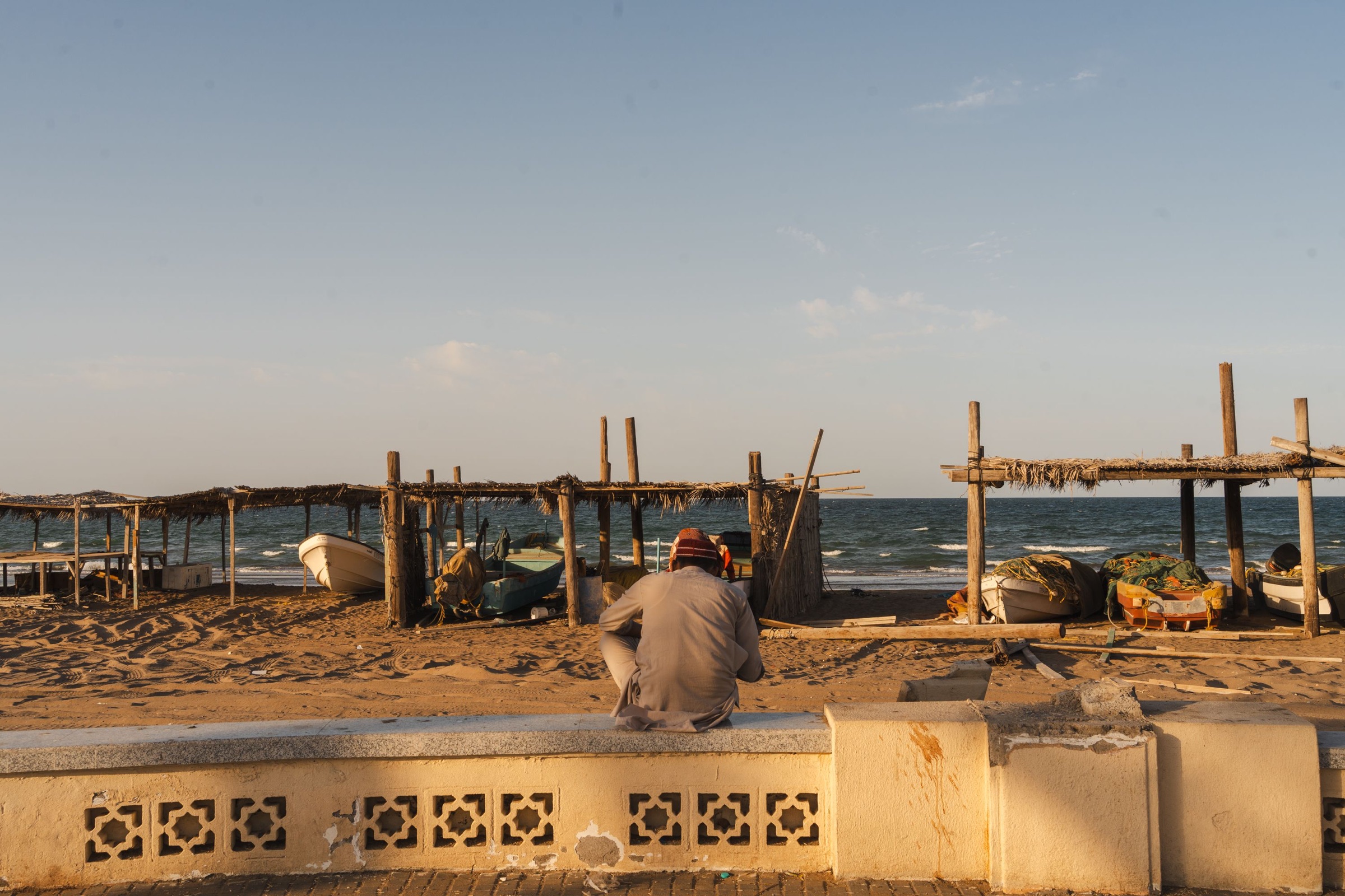 Traditional fishing shelters and boats on an Omani beach at sunset